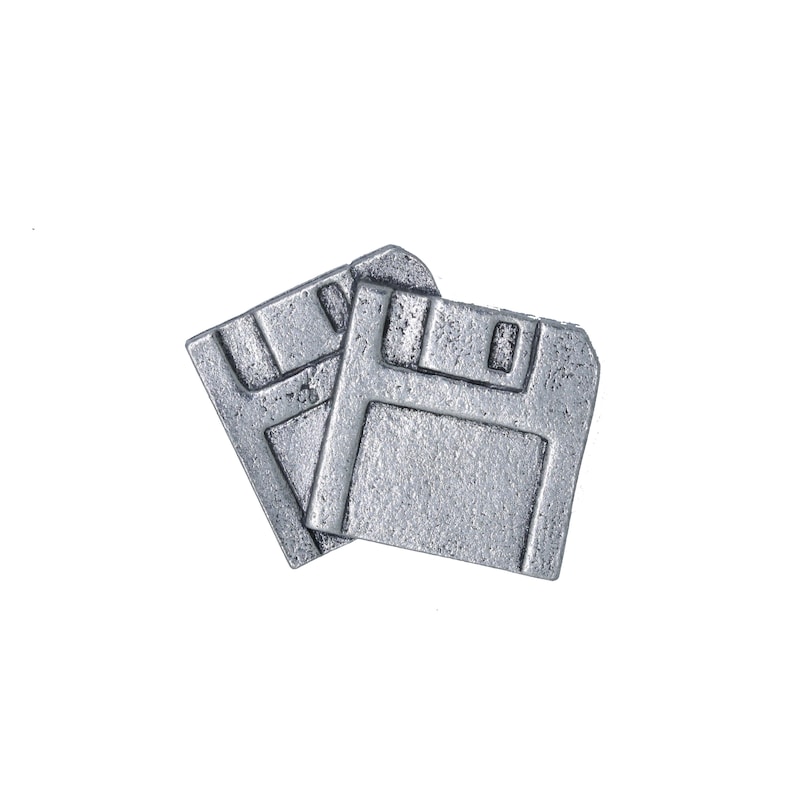 May include: Two silver-colored floppy disk pins. The pins are made of a textured metal and are slightly overlapping. The design is a retro nod to vintage computer technology and data storage.