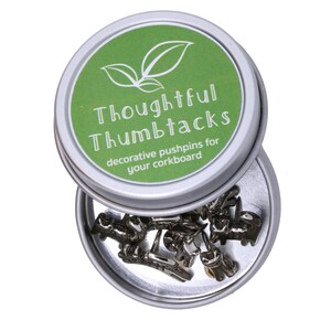 May include: A silver tin with a green lid that says "Thoughtful Thumbtacks" and "decorative pushpins for your corkboard". The tin is open and contains silver thumbtacks.