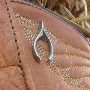 May include: A brown leather boot with a silver horseshoe charm. The boot has decorative stitching and a pointed toe.