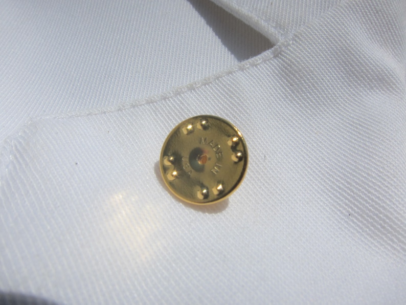 May include: A gold-colored metal pin with the text "MADE IN THE USA" on the back.