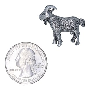 May include: A silver-colored pewter goat figurine, standing on a white background. The goat is about the size of a US quarter.