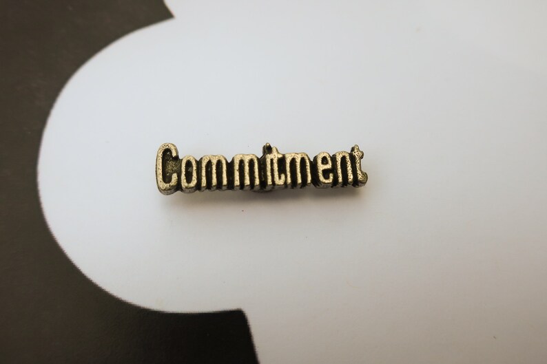 May include: A gold-colored metal charm with the word "Commitment" embossed on it.