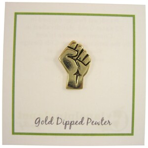 May include: Gold-dipped pewter pin featuring a raised fist with an arrow pointing upwards. The pin is on a white card with the text "Gold Dipped Pewter".