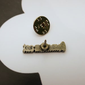 May include: Silver-toned metal pin with the text "GIFT" in raised letters. The pin has a back post and a butterfly clutch.