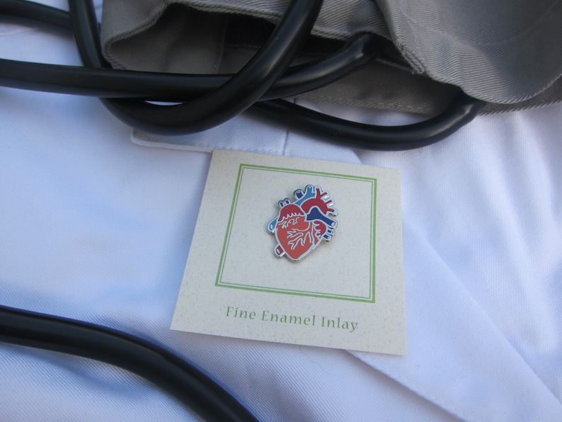 May include: A red, blue and white enamel heart pin on a white background. The pin is on a card that says "Fine Enamel Inlay".