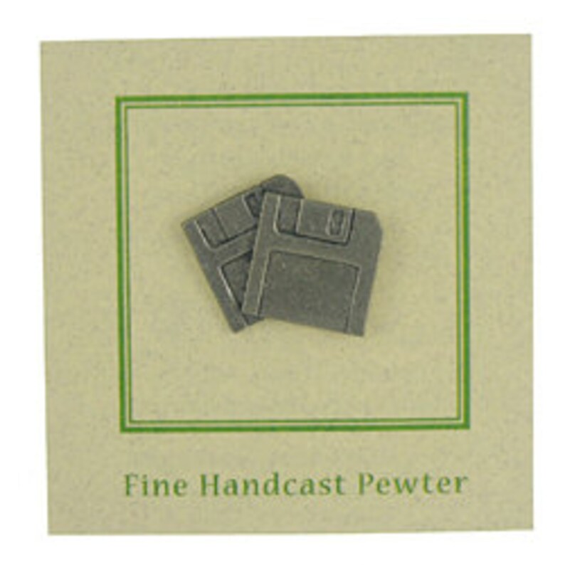 May include: Two small, gray pewter floppy disk pins on a beige card with a green border. The text "Fine Handcast Pewter" is printed in a dark green font below the pins. The pins are a retro design.