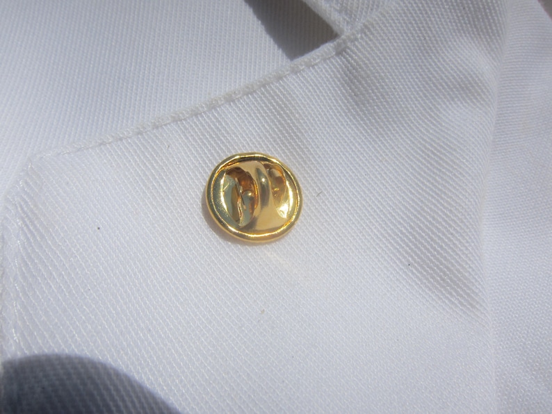 May include: A gold-colored pin with a rounded shape.