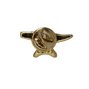 May include: Gold-colored metal pin with a stylized airplane design. The pin has a safety clasp on the back.