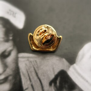 May include: Gold-toned pin with a circular design. The pin has a safety clasp on the back.