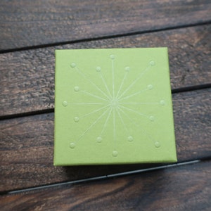 May include: A green box with a white starburst design. The box is made of a textured material.