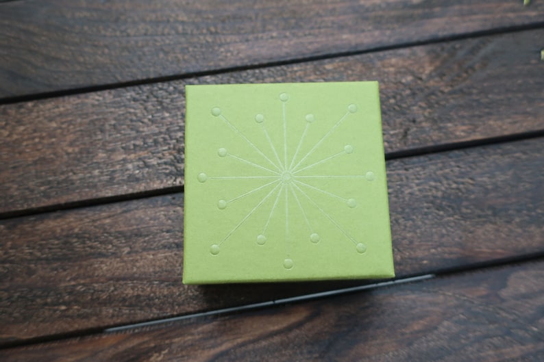 May include: A green box with a white starburst design. The box is made of a textured material.