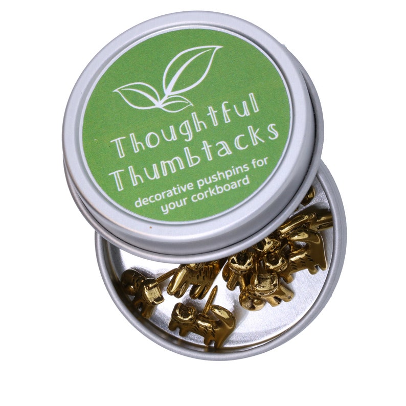 May include: A silver tin with a green lid that says "Thoughtful Thumbtacks decorative pushpins for your corkboard". The tin is open and filled with gold thumbtacks shaped like elephants.