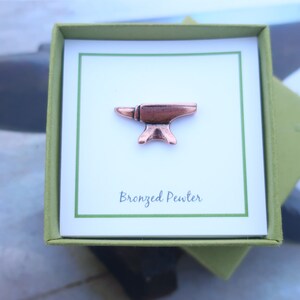May include: A small, bronze-colored pewter anvil pin in a green gift box with a white card that says "Bronzed Pewter".