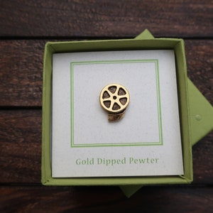 May include: A gold-dipped pewter film reel pin in a green box with a white card that says "Gold Dipped Pewter".
