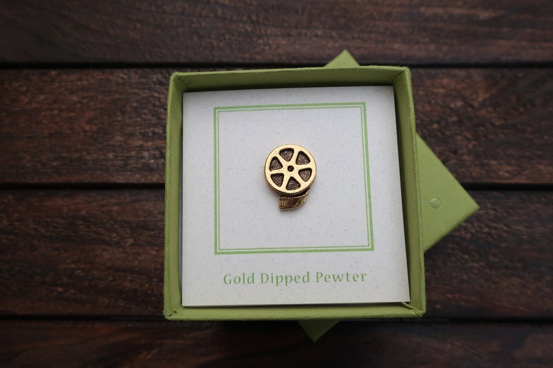 May include: A gold-dipped pewter film reel pin in a green box with a white card that says "Gold Dipped Pewter".