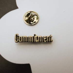 May include: A gold-colored metal pin with the word "Commitment" embossed on it.