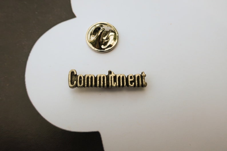 May include: A gold-colored metal pin with the word "Commitment" embossed on it.