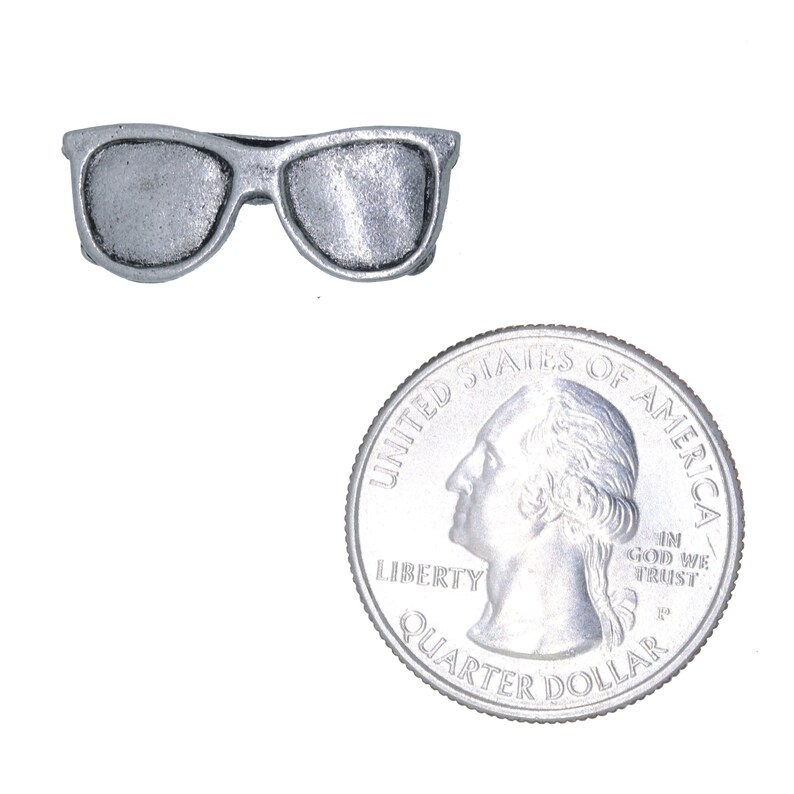 Puede incluir: Un amuleto de plata con forma de gafas de sol, del tama&ntilde;o de una moneda de 25 centavos de d&oacute;lar estadounidense.