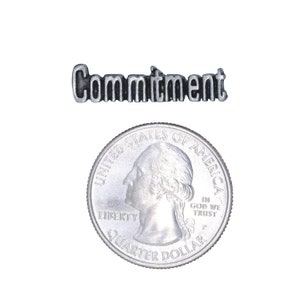 May include: A silver charm with the word "Commitment" engraved on it. The charm is about the size of a US quarter.