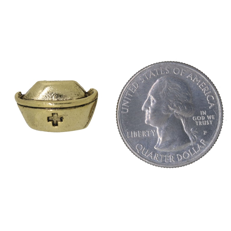 May include: A gold-colored nurse's cap charm with a red cross in the center. The charm is about the size of a US quarter.