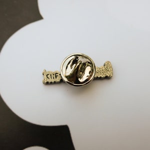 May include: A silver pin with the word "Love" written in a stylized font. The pin has a circular back with a safety clasp.