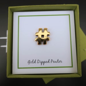 May include: A gold-dipped pewter hashtag charm in a green gift box. The box has a white card inside with the text "Gold Dipped Pewter".