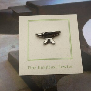 Peut inclure: Une &eacute;pingle en &eacute;tain argent&eacute; en forme d'enclume sur une carte blanche avec une bordure verte. La carte indique "Fine Handcast Pewter".