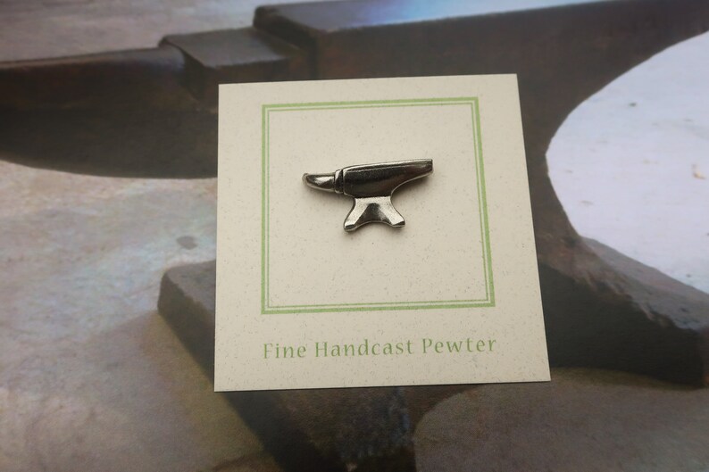 Peut inclure: Une &eacute;pingle en &eacute;tain argent&eacute; en forme d'enclume sur une carte blanche avec une bordure verte. La carte indique "Fine Handcast Pewter".