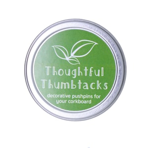 Może przedstawiać: Srebrny pojemnik z zieloną etykietą, na kt&oacute;rej widnieje napis "Thoughtful Thumbtacks" oraz "decorative pushpins for your corkboard".