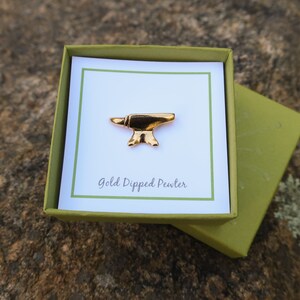 May include: A gold-dipped pewter anvil pin in a green box with a white card that says "Gold Dipped Pewter".