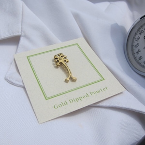 May include: A gold-colored pin shaped like a stylized tree with the text "Gold Dipped Pewter" on a white card.