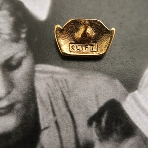 May include: Gold-toned earring with a geometric design and the word "CLIFT" engraved on the back.