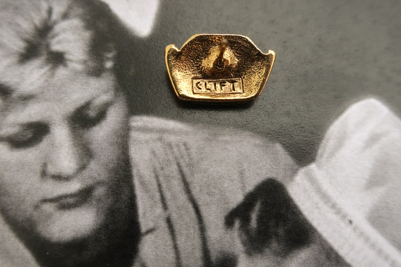 May include: Gold-toned earring with a geometric design and the word "CLIFT" engraved on the back.
