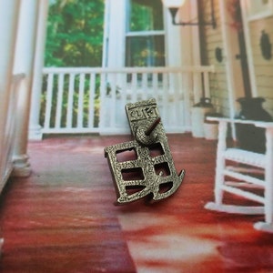 Pode incluir: Pin de metal prateado em forma de casa com a palavra "CLIFF" na frente. O pin est&aacute; sobre uma superf&iacute;cie vermelha e branca.