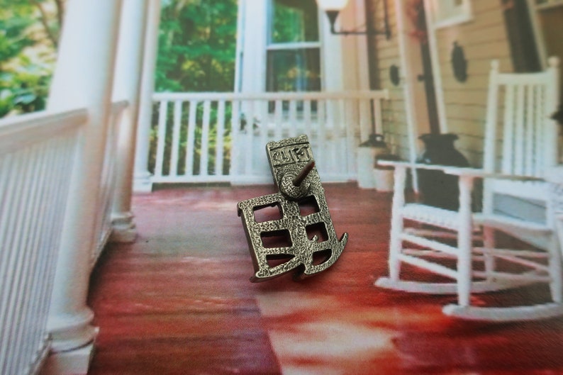 Pode incluir: Pin de metal prateado em forma de casa com a palavra "CLIFF" na frente. O pin est&aacute; sobre uma superf&iacute;cie vermelha e branca.