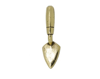 Puede incluir: Un amuleto de paleta de albañil en miniatura de color dorado. La paleta tiene una hoja puntiaguda y un mango corto.