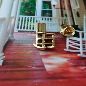 Pode incluir: Pin de cadeira de balan&ccedil;o dourado em um fundo branco mostrando uma cadeira de balan&ccedil;o em uma varanda.