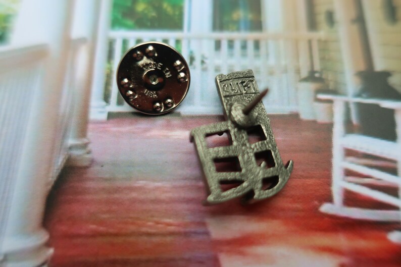 Pode incluir: Pin de metal prateado com um design detalhado de um edif&iacute;cio com a palavra "GULF" na frente. A parte de tr&aacute;s do pin tem um suporte circular de metal com as palavras "MADE IN USA".