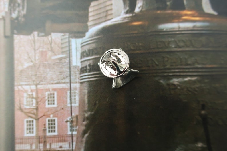 Puede incluir: Un pin de plata con un dise&ntilde;o redondo y elevado de la Campana de la Libertad. El pin est&aacute; unido a una base en forma de campana.