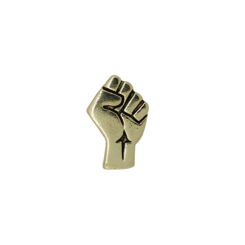 May include: A gold-colored metal pin in the shape of a raised fist.