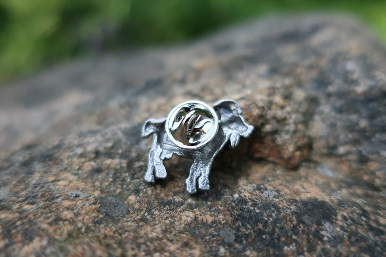 May include: Silver-toned metal pin featuring a detailed depiction of a goat. The pin has a safety clasp on the back.