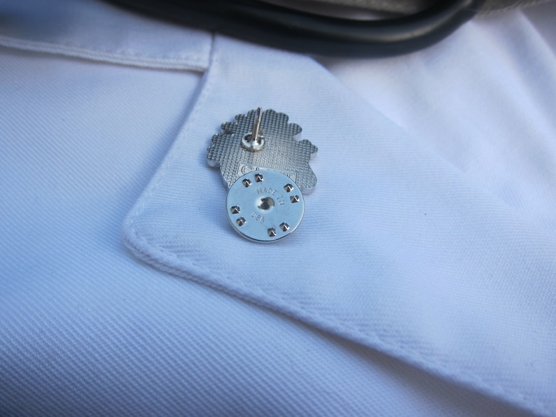 May include: A silver pin featuring an intricate flower design. The reverse side of the pin displays the text "MADE IN ITALY" on a circular metal piece.