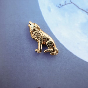 May include: A gold-colored wolf pin with a detailed design. The wolf is howling at the moon.