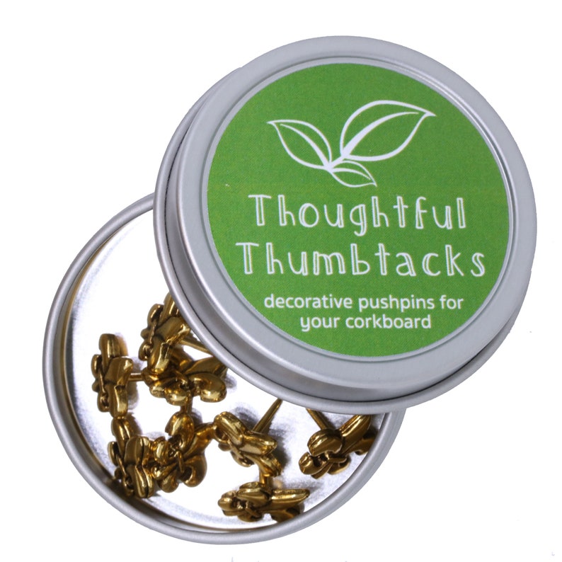 Może przedstawiać: Srebrny pojemnik z zieloną pokrywką zawierający złote pinezki. Pokrywka ma zielony wz&oacute;r liści i tekst "Thoughtful Thumbtacks decorative pushpins for your corkboard".