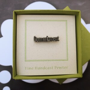 May include: A pewter pin in a green box with a white background. The pin says "Commitment" and "Fine Handcast Pewter".