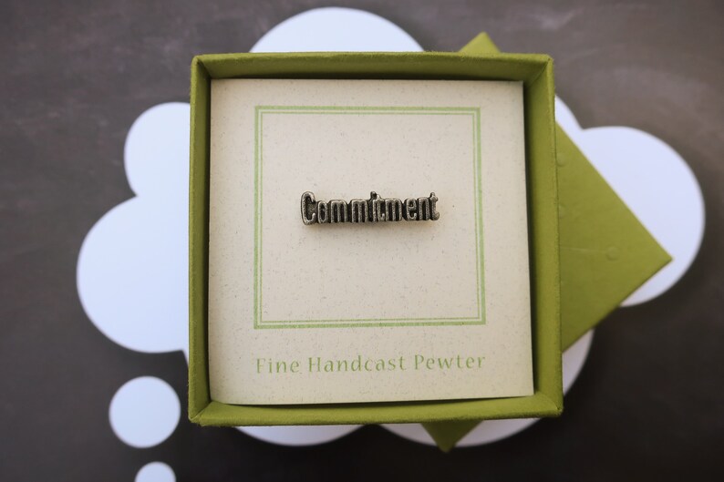 May include: A pewter pin in a green box with a white background. The pin says "Commitment" and "Fine Handcast Pewter".