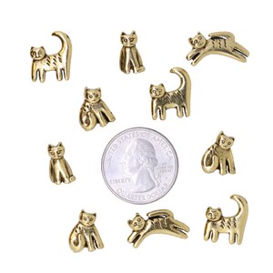May include: Ten gold-colored metal cat figurines of various poses, including sitting, standing, and jumping. The figurines are about the size of a US quarter.