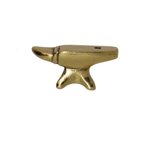 May include: A small, gold-colored metal anvil with a rounded top and a small hole in the center. The anvil has a three-legged base.