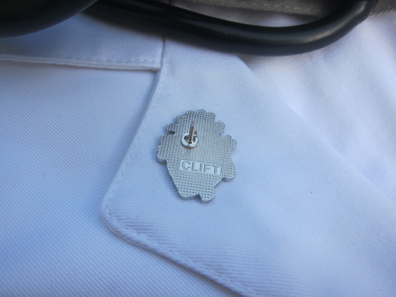 May include: A silver heart-shaped pin with the word "CLIFT" embossed on it.