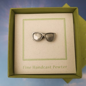 Puede incluir: Un alfiler de gafas de sol de peltre plateado en una caja verde con el texto "Fine Handcast Pewter".